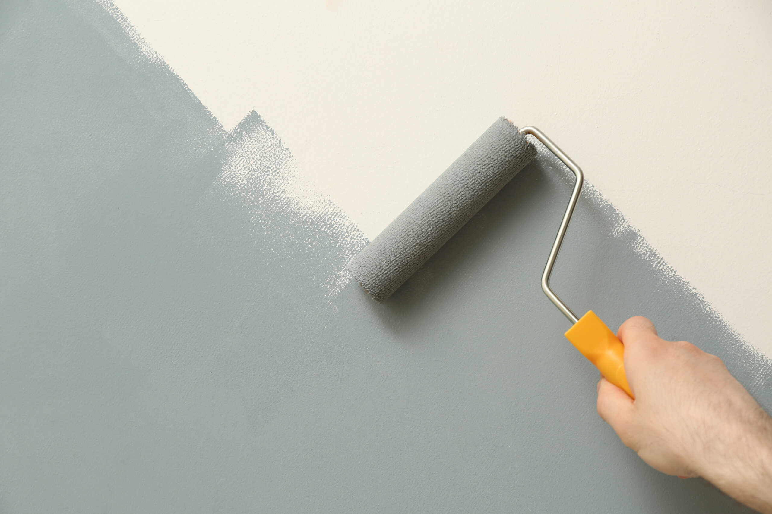 Man applying grey paint with roller brush on white wall, closeup